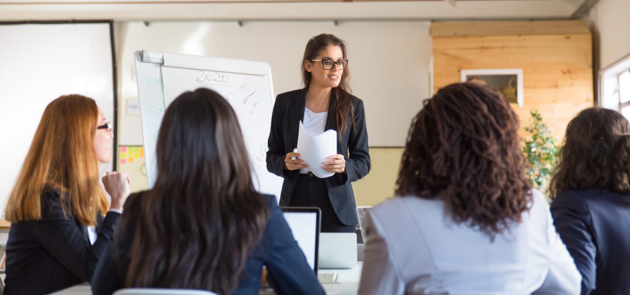 Businesswomen looking at speaker with papers. Group of professional multiethnic businesswomen looking at leader during meeting in office. Women in business concept